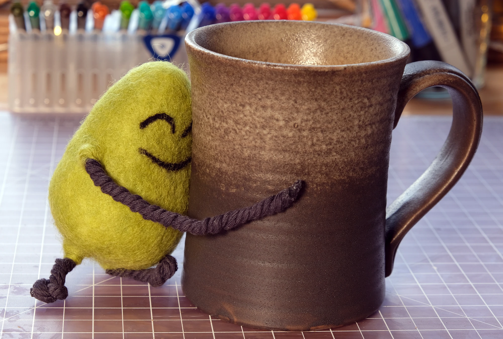 A felted Cloudia hugging a mug of coffee as tall as she is.