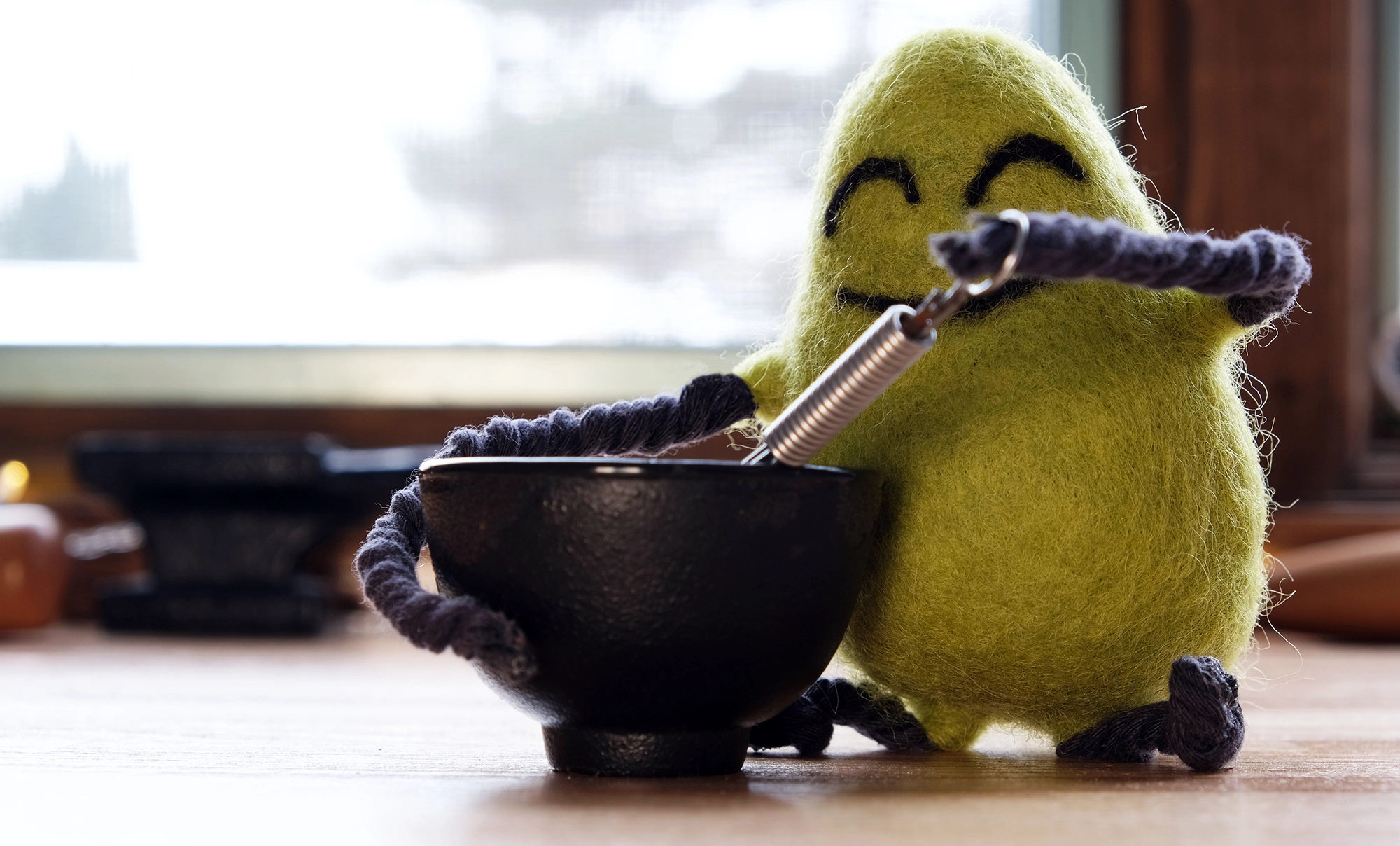 A felted Cloudia holding a tiny whisk and bowl.