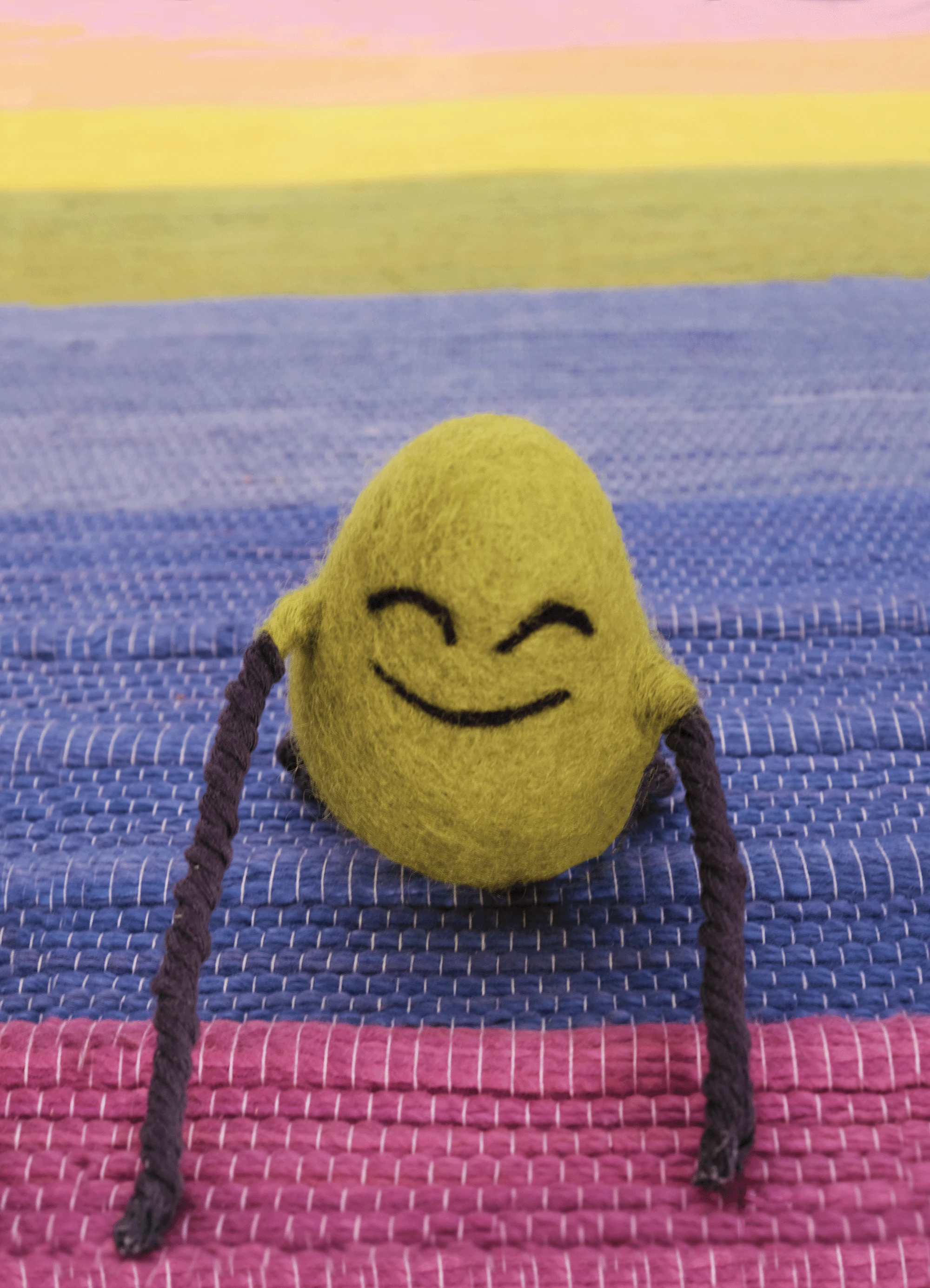 A felted Cloudia doing yoga on a rainbow mat.